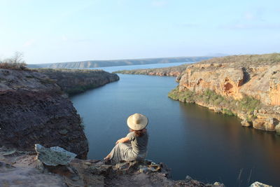 Rear view of woman sitting on rock by sea against sky