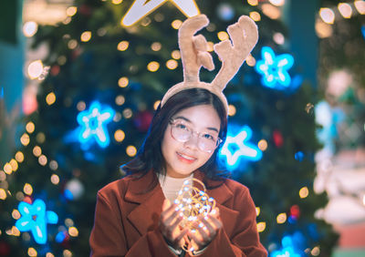 Portrait of young woman holding illuminated string lights