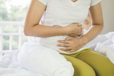 Midsection of woman with stomachache kneeling on bed at home