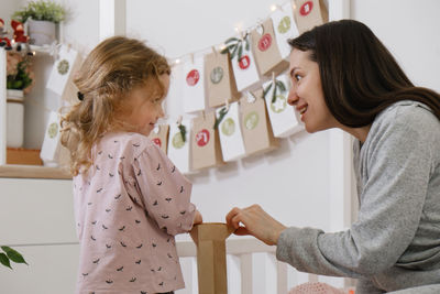 Mother with child opening christmas advent calendar tasks and gifts. toddler girl excited about