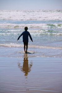 Rear view of man standing on beach against sky