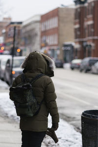 Rear view of person standing on sidewalk in city during winter