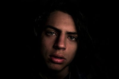 Close-up portrait of young woman against black background