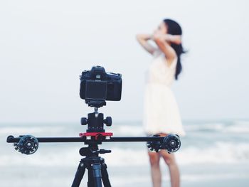 Close-up of camera with woman standing in background at beach