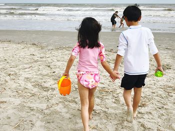 Rear view of siblings holding hands while walking at beach