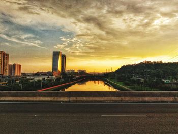 Bridge over river by buildings against sky during sunset