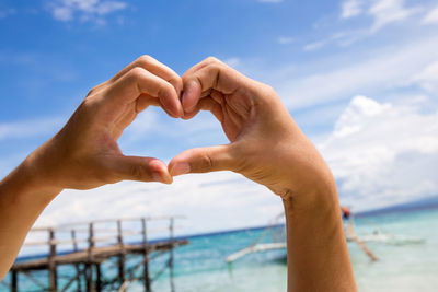 Close-up of hands making heart shape against sea