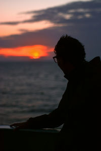 Silhouette man sitting on beach against sky during sunset