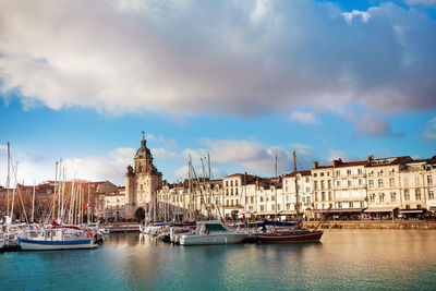 Sailboats in city against cloudy sky