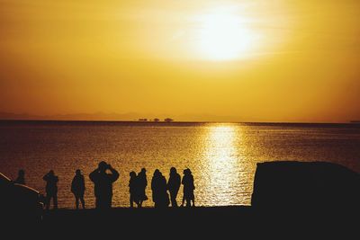 Silhouette people by sea against sky during sunset