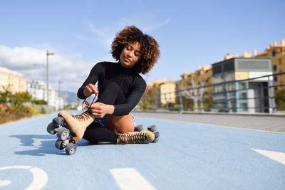 Woman wearing roller skate while sitting on road in city
