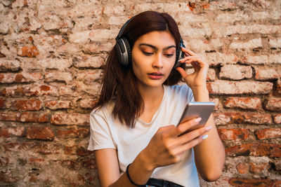 Beautiful young woman using mobile phone against brick wall