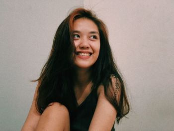 Portrait of smiling young woman against wall