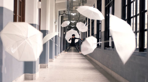 Young woman with umbrellas in mid-air at corridor