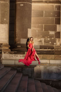 Full length of woman wearing red evening gown against building
