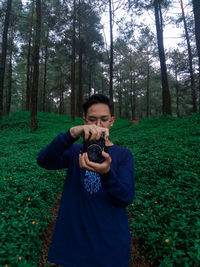 Front view of man holding camera in forest