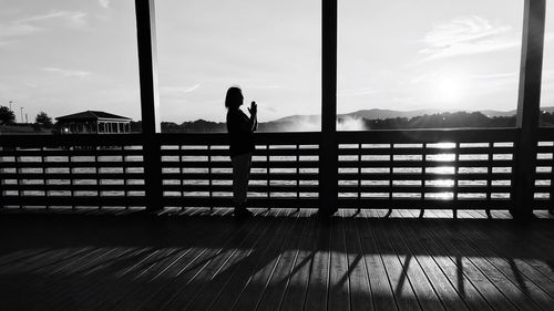 Silhouette woman standing with hands clasped by railing against sky