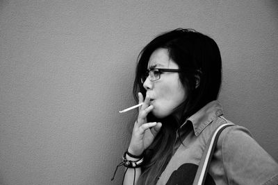Portrait of young woman smoking cigarette against wall