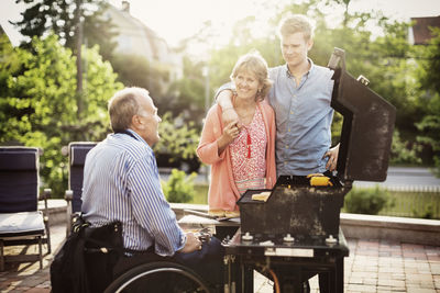 Family looking at disabled man barbecuing at yard