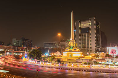 Illuminated modern buildings by street against sky at night