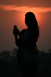 Silhouette woman using mobile phone against orange sky during sunset