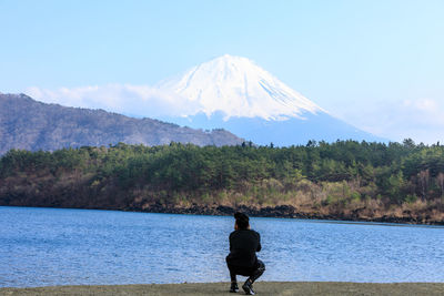 Rear view of man standing on mountain by lake against sky