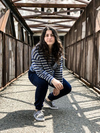 Portrait of young woman crouching at footbridge