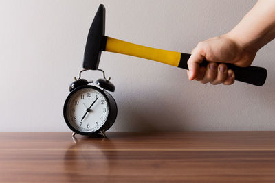 Close-up of hand holding clock on table against wall