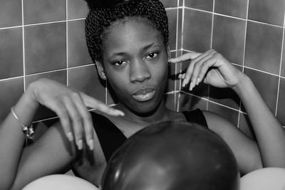 Portrait of young woman sitting against tiled wall