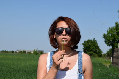 Young woman blowing dandelion while standing on field during sunny day