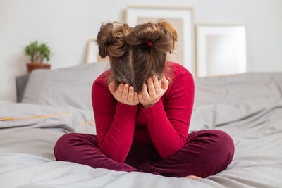 Rear view of woman sitting on bed at home