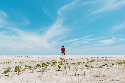 Rear view of man sitting on chair on land against sky