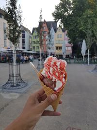 Close-up of hand holding ice cream cone against buildings
