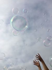 Low angle view of cropped hands and bubbles against sky