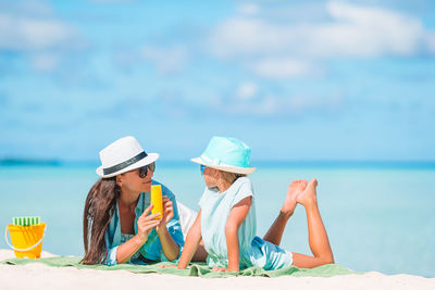 Mother and daughter wearing hat lying down on beach