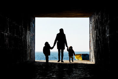 Silhouette woman with children walking on beach against sky