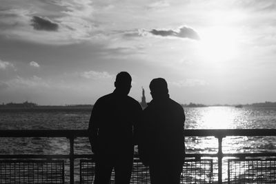 Rear view of silhouette men looking at statue of liberty against sky