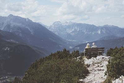 Man and woman resting on bench at observation point against mountains