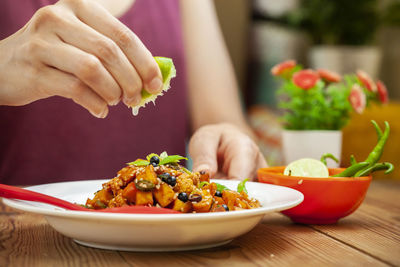 Midsection of person holding vegetables in bowl on table