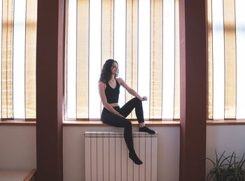 Young woman looking away while sitting on window at home