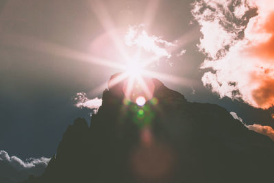 Low angle view of sun streaming through clouds during sunset