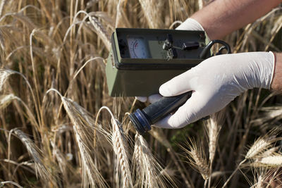 Cropped image of man holding geiger counter on field