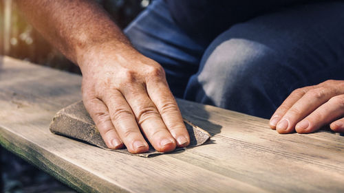 Midsection of carpenter sanding wooden plank at carpentry