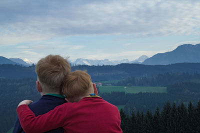 Rear view of siblings looking at mountains against sky