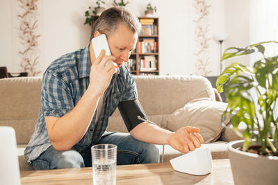 A man measures blood pressure at home with a blood pressure cuff and a tonometer. 