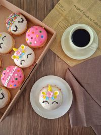 A box of donuts, a donut on a plate and a cup of black coffee on the table