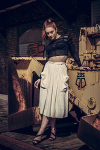 Young woman standing against rusty bulldozer in city