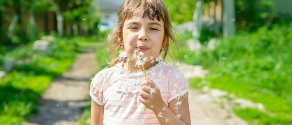 Smiling girl blowing dandelion on sunny day