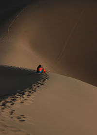 Rear view of woman sitting on desert during sunset