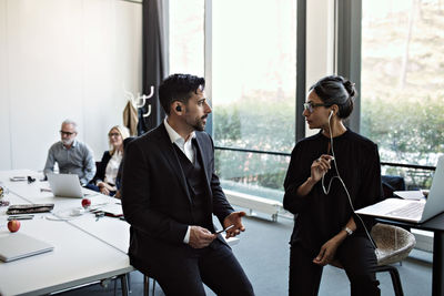 Businessman discussing to businesswoman using laptop with colleagues working at conference table in board room